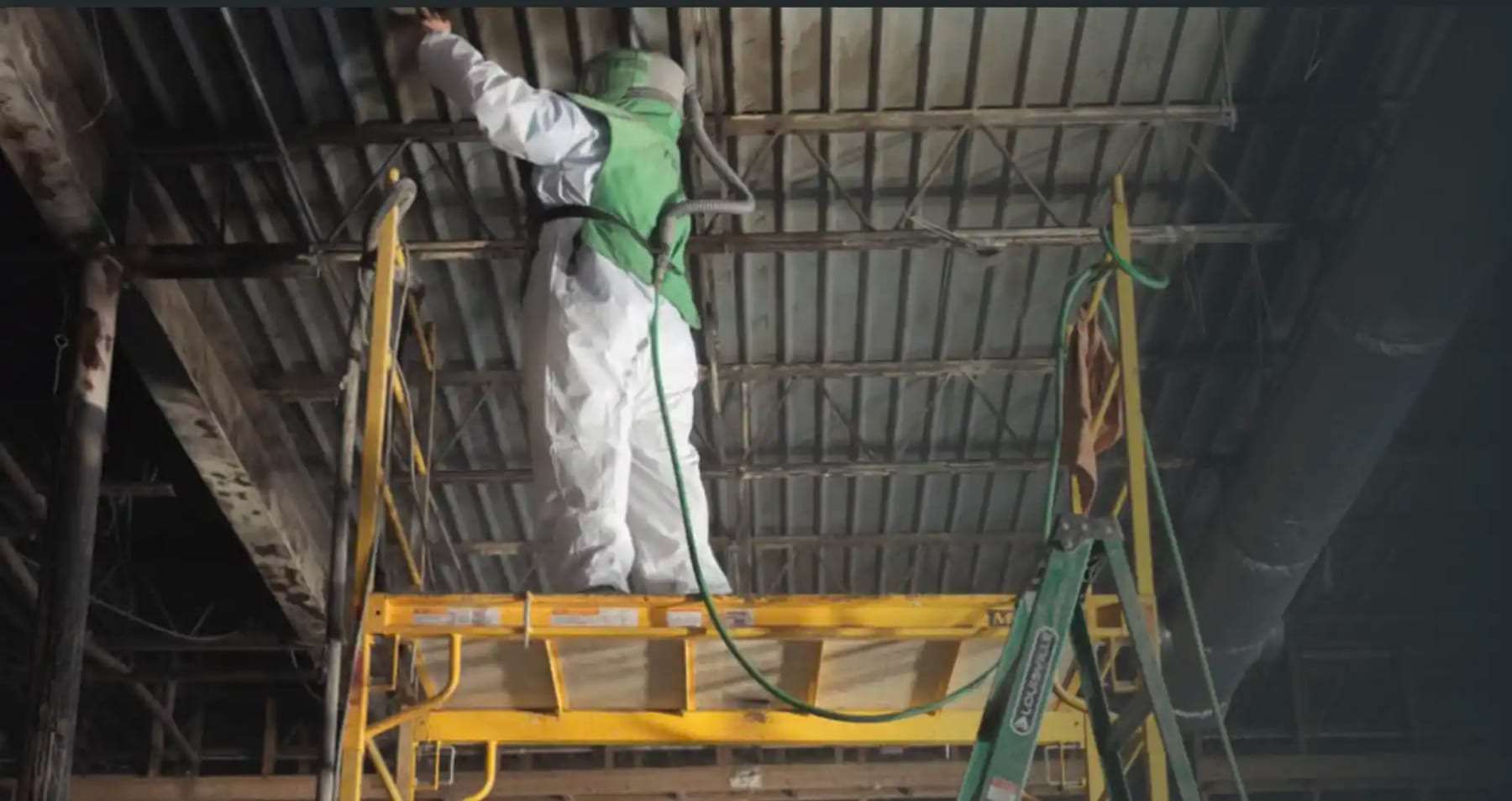 Technician on a ladder spraying the underside of a warehouse roof deck